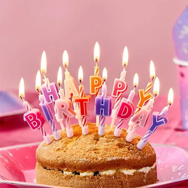 Birthday cake with colourful Happy Birthday letter candles lit against a pink party-themed background.